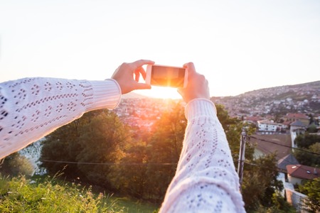 Woman taking photograph of sunset with mobileの写真素材