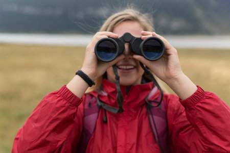young blonde woman hiking and watching through binoculars.