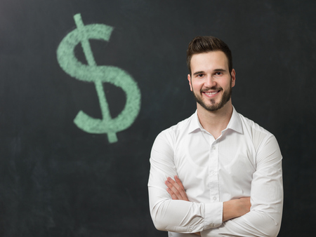 Happy  man standing in front of dollar sign written on a chalkboard.の写真素材