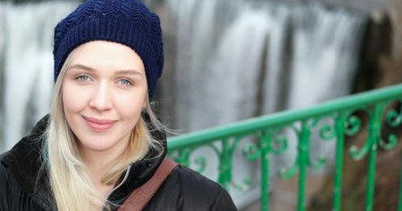Outside portrait of beautiful blonde girl wearing beanie and coat. Nature background. Looking at...