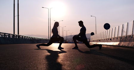 Silhouette of a fitness couple profile stretching at sunset with the sun in the backgroundの写真素材