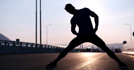 Silhouette of a fitness man profile stretching at sunset with the sun in the backgroundの写真素材