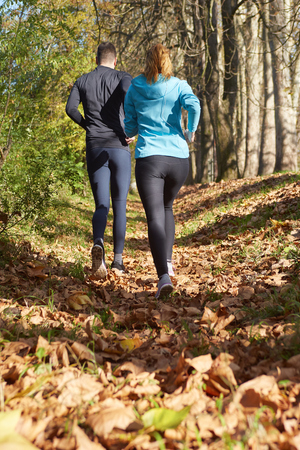 Young running couple jogging in autumn natureの写真素材
