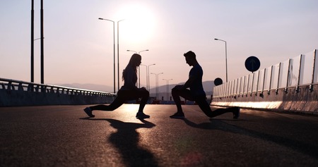 Silhouette of a fitness couple profile stretching at sunset with the sun in the backgroundの写真素材
