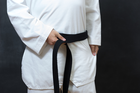 karate man tying the knot to his black belt on black backgroundの写真素材