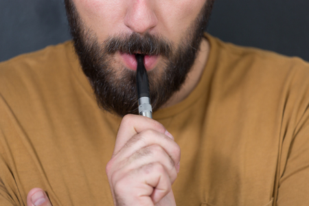 Man with concealed identity smoking a controversial vaping an electronic cigarette. Vaping is debatable in the health community if it is safe or a health riskの写真素材