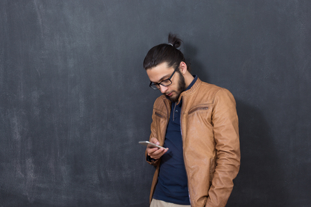 Casually handsome. Handsome young arabic man holding cell phone while standing against grey backgroundの写真素材