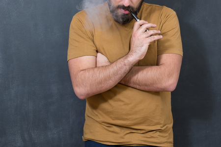 Black haired handsome man vaping e-cirarette mod - blowing cloud of vaporの写真素材