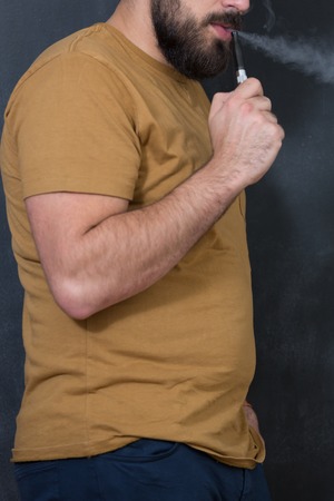 Closeup of man using e-cigarette and exhaling vapor shot over black backgroundの写真素材