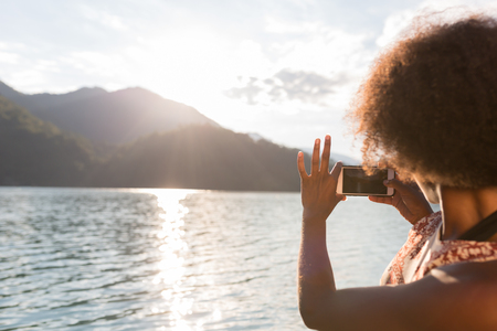 Wonderful sunset over hills, tourist taking a picture of the lake. Afro american woman visiting Europe.の写真素材