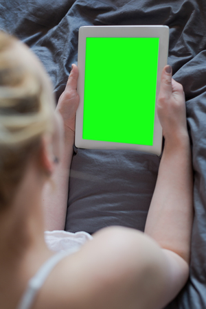Beautiful emotional young woman using tablet computer with empty screen in her bedroomの写真素材