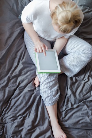 Woman lying in bed with digital tablet touching with finger. View from aboveの写真素材