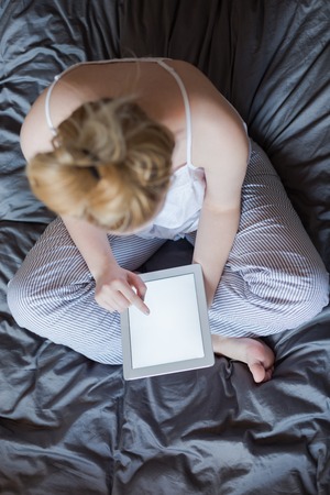 Woman using tablet at cozy home atmosphere on the bed. Young beautiful woman enjoying free time using technological deviceの写真素材