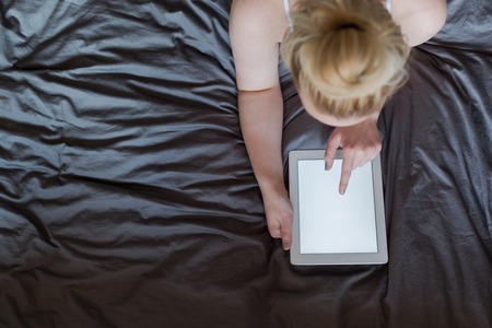 Beautiful emotional young woman using tablet computer with empty screen in her bedroomの写真素材