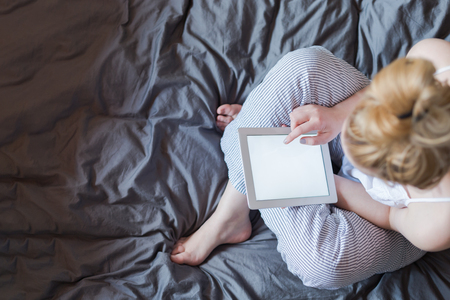 Beautiful emotional young woman using tablet computer with empty screen in her bedroomの写真素材