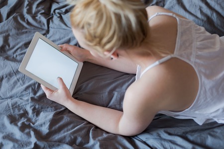 Beautiful emotional young woman using tablet computer with empty screen in her bedroomの写真素材