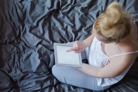 Beautiful emotional young woman using tablet computer with empty screen in her bedroomの写真素材