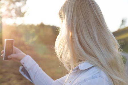 Woman taking a selfie in nature during the sunsetの写真素材