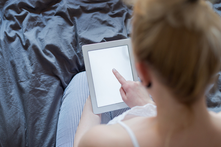 Beautiful emotional young woman using tablet computer with empty screen in her bedroomの写真素材