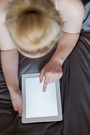 Beautiful emotional young woman using tablet computer with empty screen in her bedroomの写真素材
