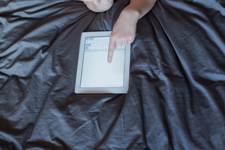 Beautiful emotional young woman using tablet computer with empty screen in her bedroomの写真素材