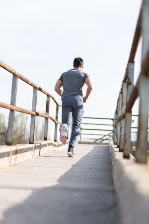 Full length portrait of handsome runner jogging fast down the bridge in urban setting with copy space area for your text message or content, young male jogger working out outdoorsの写真素材