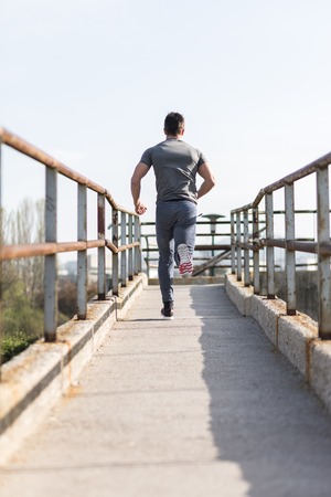 Sporty young man working out at early morning while run up the bridge  on background, male jogger exercisingの写真素材