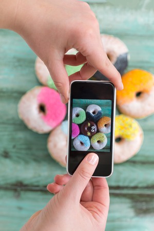 Overhead of feminine hands using smartphone, coffee and donut on tableの写真素材
