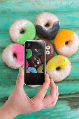 Overhead of feminine hands using smartphone, coffee and donut on tableの写真素材