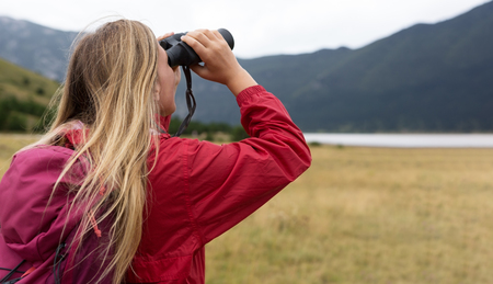 young blonde woman hiking and watching through binoculars.の写真素材