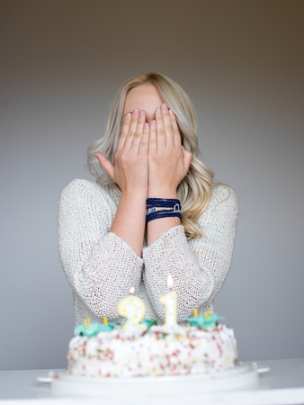 Portrait of a young beautiful blond girl holding plate with birthday cake and blowing candles making a wishの写真素材