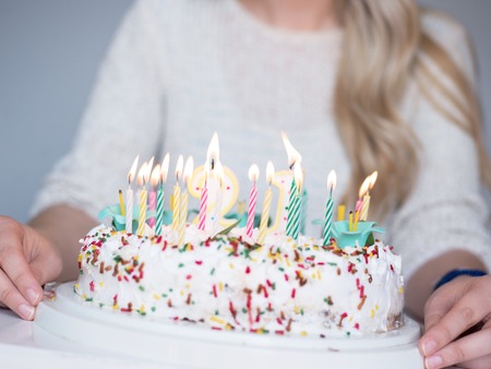 Portrait of a young beautiful blond girl holding plate with birthday cake and blowing candles making a wishの写真素材