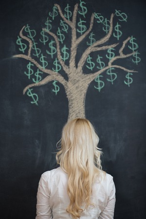 Happy blonde Business woman in front of chalk money tree drawing on blackboard.の写真素材