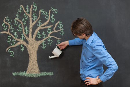 Photo of young businessman on chalkboard background. Dollar tree painted on chalkboard growing from the headの写真素材