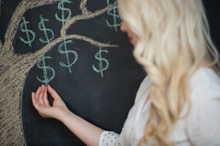 Happy blonde Business woman in front of chalk money tree drawing on blackboard.の写真素材