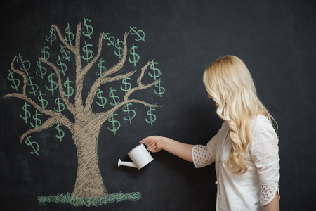 Happy blonde Business woman in front of chalk money tree drawing on blackboard.の写真素材