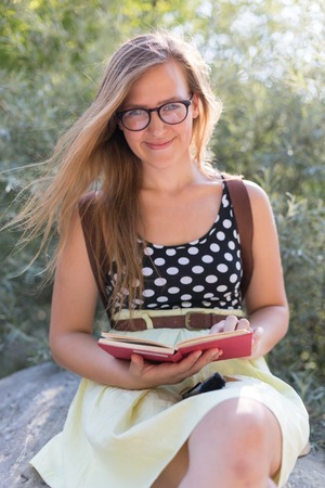 Cute young woman sitting on rocks and reading the book in natureの写真素材