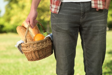 A young man holding a basket with a blanket, baguette and coffee. Autumn picnic in the park.の写真素材