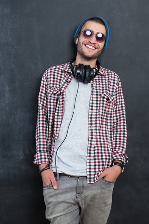 Carefree music lover. Joyful young man in headphones smiling against chalkboard backgroundの写真素材