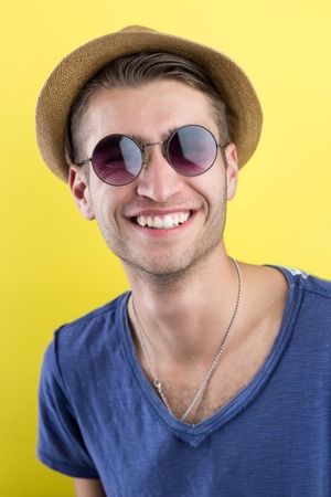 Cheerful young man in hat and sunglasses over yellow backgroundの写真素材