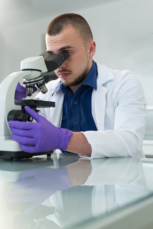 Young scientist investigating microbiological substance in microscopeの写真素材