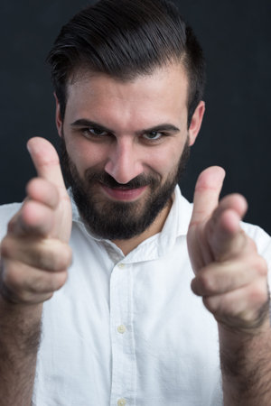 Portrait of a  young bearded man pointing to camera against black chalkboard