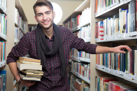 Smiling male student picking a book in a library