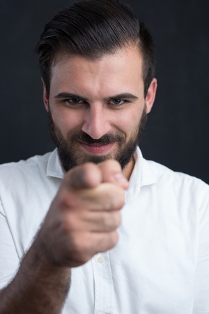 Portrait of a  young bearded man pointing to camera against black chalkboardの写真素材