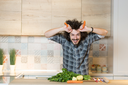 Handsome man cooking vegetable salad in kitchen and holding carros as  hornesの写真素材