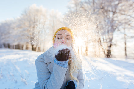 Winter girl blowing snow in frosty winter park, young woman having fun in winter park. Sunset shot with selective focusの写真素材