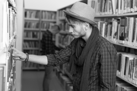 male college student taking book from shelf in library.の写真素材