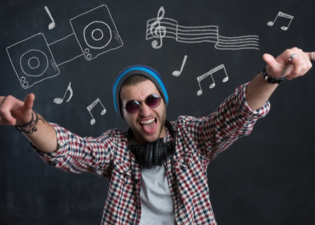 Pretty smiling young man with sunglasses listening music in headphones with musically drawingsの写真素材