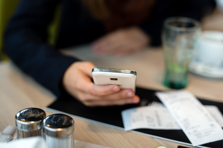 Close up of a typing on a phone in a coffee shop.の写真素材