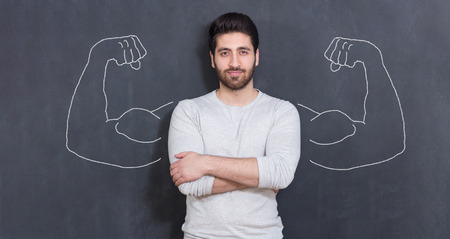 Young man against the background of depicted muscles on chalkboardの写真素材
